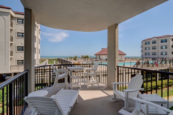 A balcony with white Adirondack chairs, a pool, and a view of the ocean.