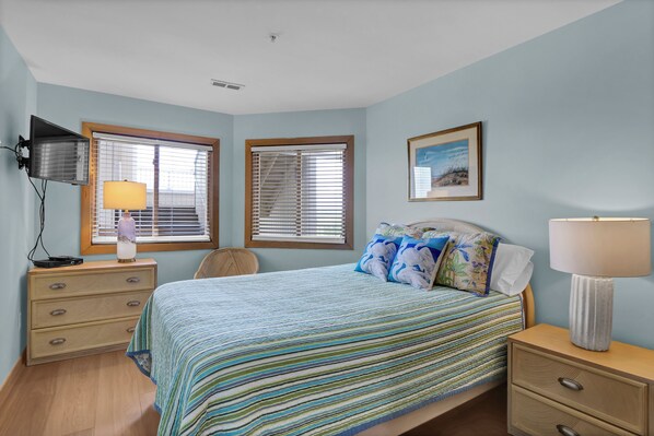 Une chambre à coucher avec un lit, deux tables de chevet, une lampe, un téléviseur et deux fenêtres.