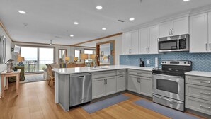A modern kitchen with stainless steel appliances, white cabinetry, and a large island. - Wrightsville Dunes F-2B - Oceanfront condo with community pool, tennis, beach (Wrightsville Beach)
