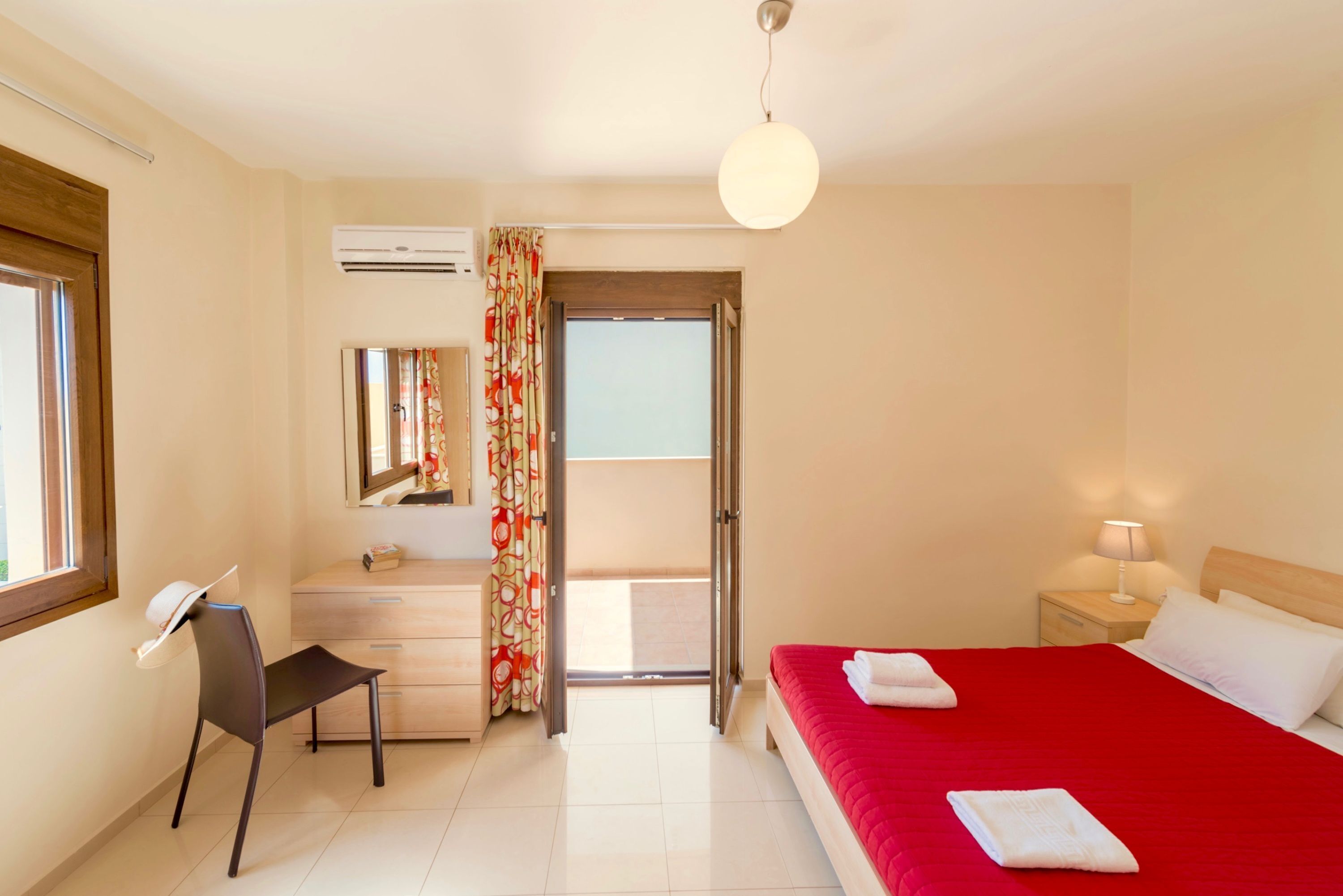 A hotel room with a bed, a desk, a chair, a mirror, a nightstand, and a window.