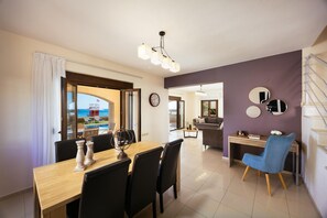 A dining area with a view of the sea, a living room with a sofa and a coffee table, and a staircase.