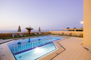 A swimming pool with a view of the sea, surrounded by lounge chairs and umbrellas. - Villa Avra (Rethymno)