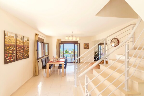 A spacious living area with a dining table, a staircase, and a view of the outdoors. - Villa Avra (Rethymno)