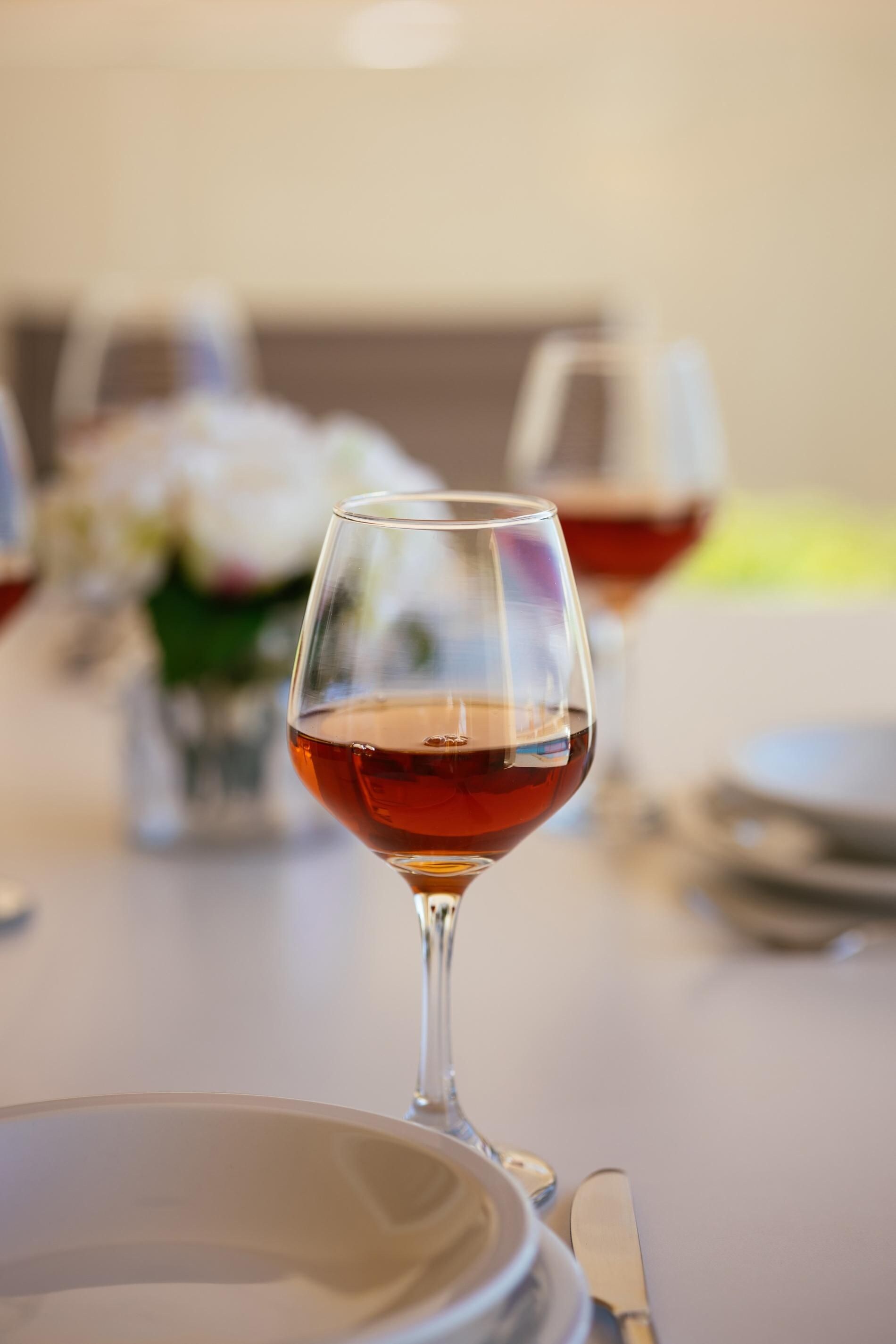 A dining table with a glass of red wine, a white plate, and a fork.