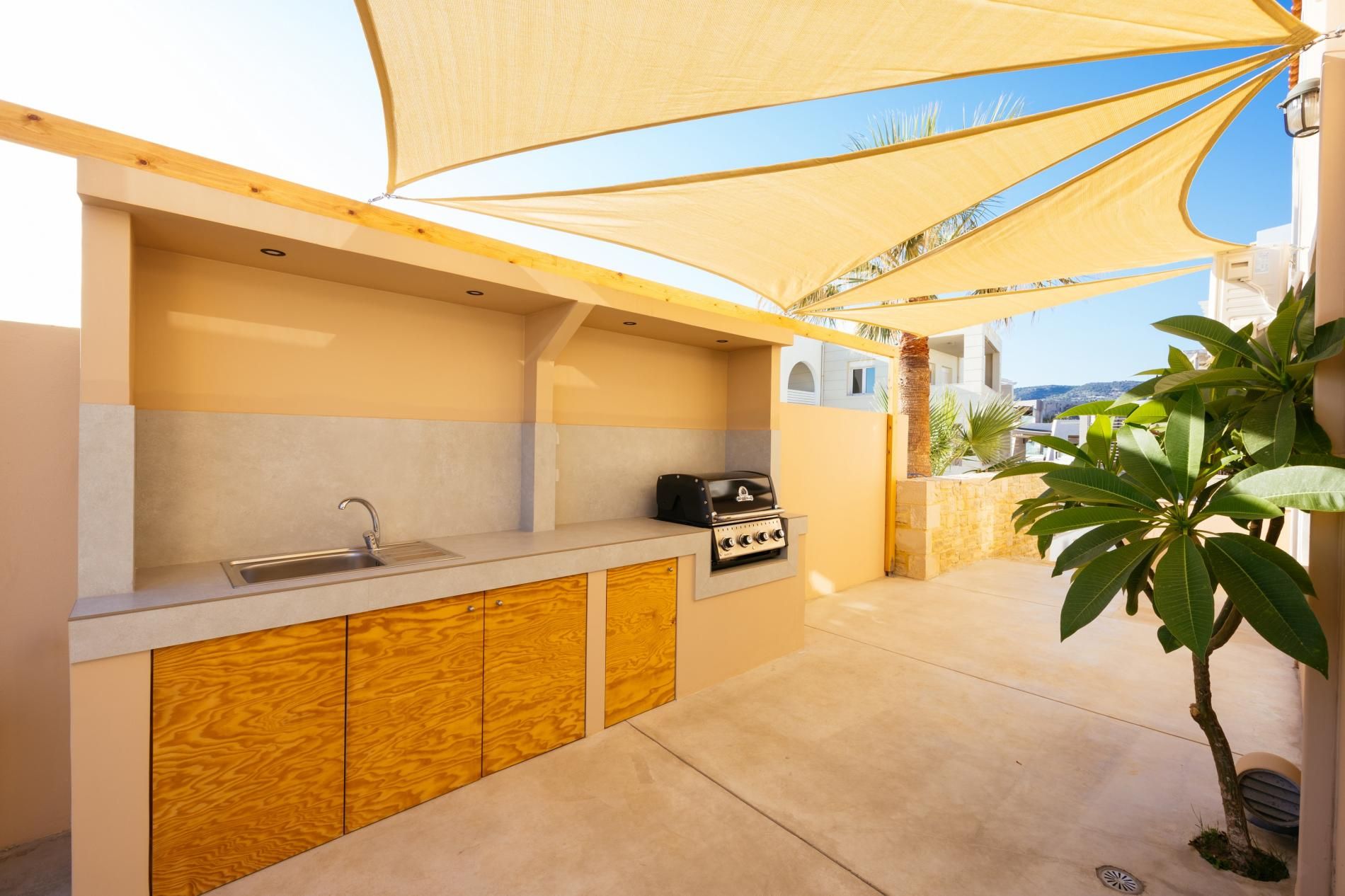 An outdoor kitchen area with a sink, a grill, and a wooden cabinet.