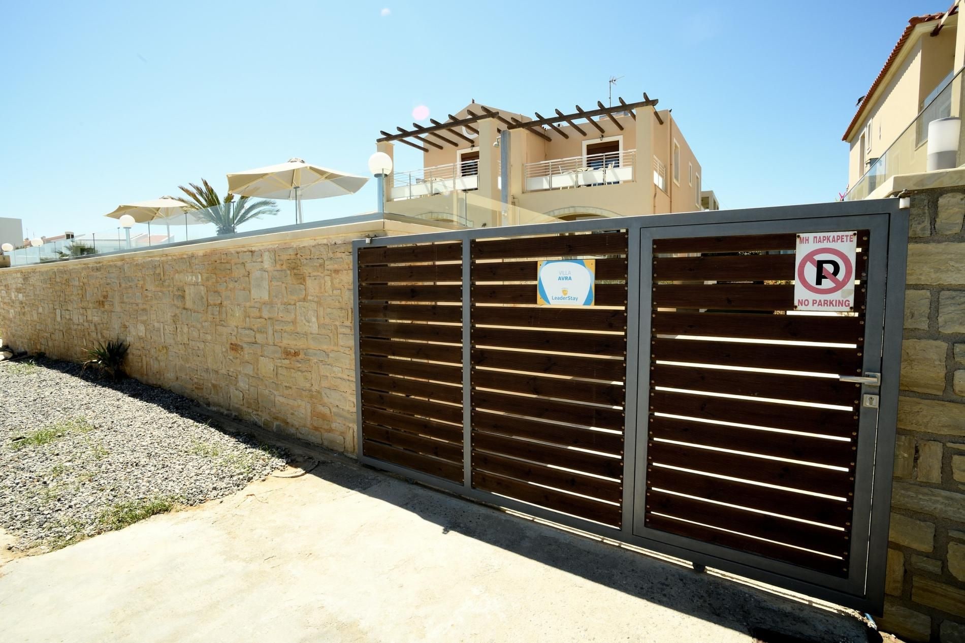 A gated entrance with a no parking sign, a LeaderStay sign, and a stone wall.