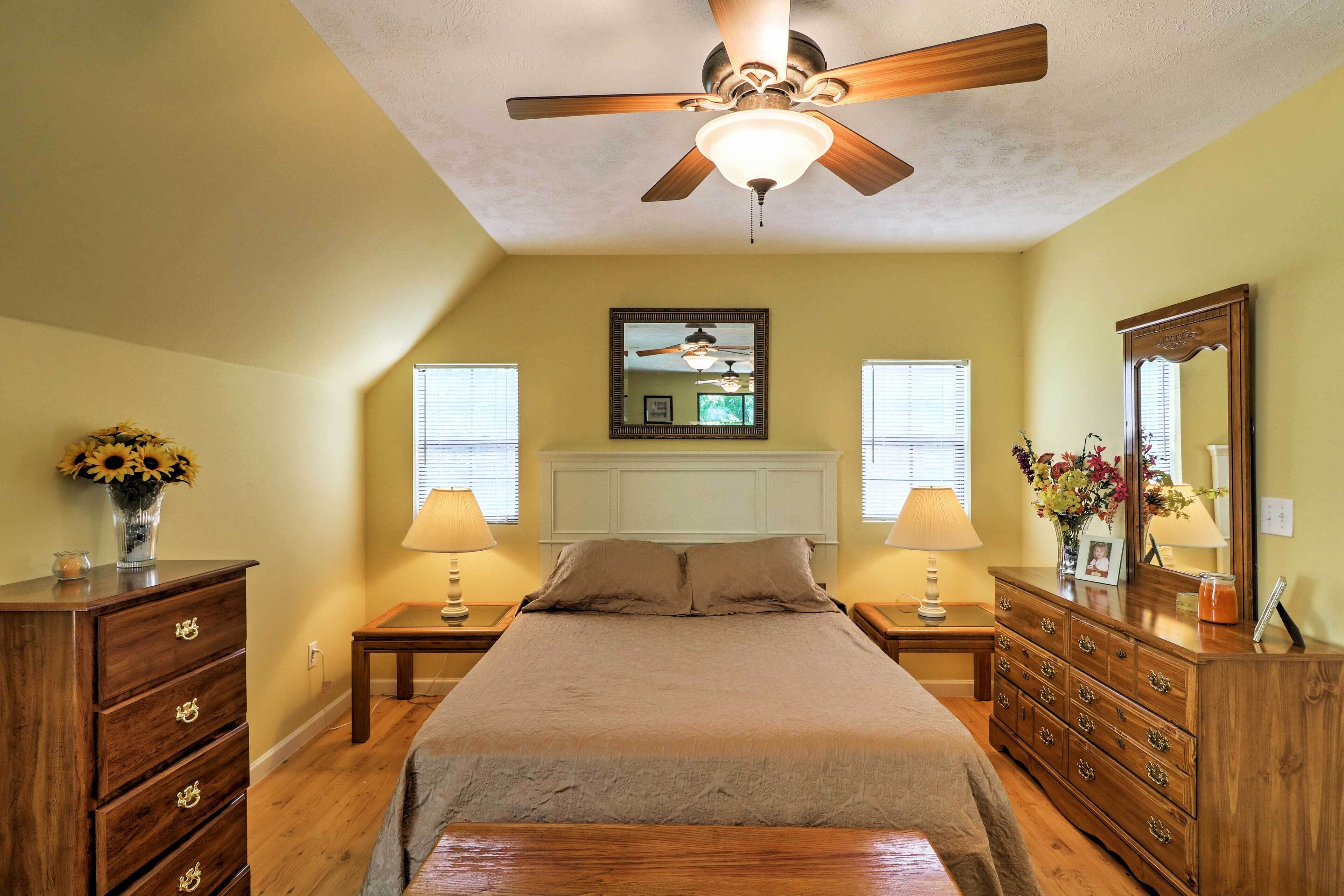 A bedroom with a bed, wooden dresser, nightstands, lamps, a ceiling fan, and a mirror.