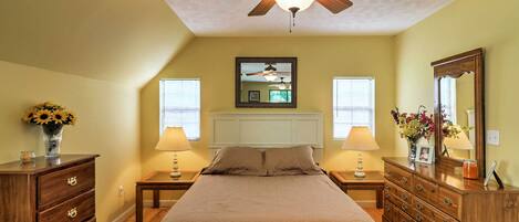 A bedroom with a bed, wooden dresser, nightstands, lamps, a ceiling fan, and a mirror.