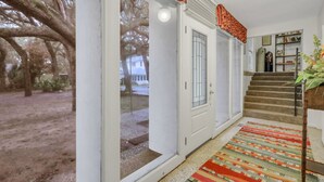 A spacious hallway with a large glass door leading to a garden, a staircase with a patterned rug, and a bookshelf with decorative items. - Beachfront Bliss 4 bedrooms, 3 bathrooms (Jekyll Island)