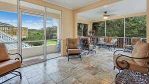 A sunlit patio with a glass door leading to a balcony, furnished with leather chairs and a table, overlooking a residential area. - Beachfront Bliss 4 bedrooms, 3 bathrooms (Jekyll Island)