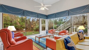 A spacious room with large windows, a ceiling fan, and a mix of red and yellow furniture. - Beachfront Bliss 4 bedrooms, 3 bathrooms (Jekyll Island)