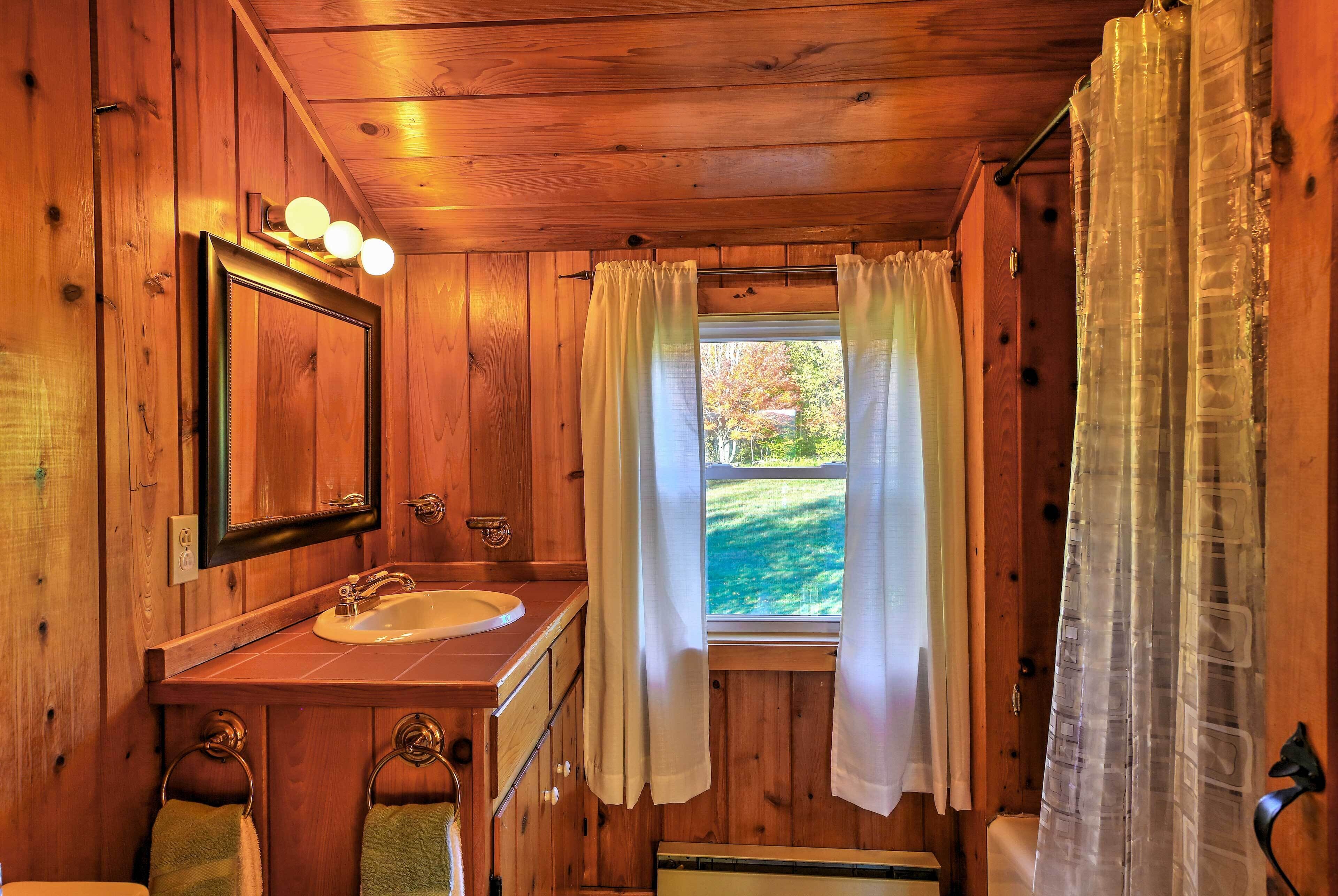 Bagno di una baita in legno con lavandino, specchio e finestra con tende.