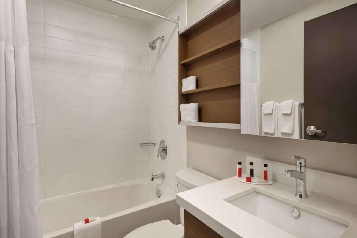 A bathroom with a bathtub, a sink, a mirror, and shelves with towels.