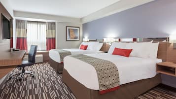 Ein Hotelzimmer mit zwei Betten, einem Schreibtisch, einem Stuhl und einem großen Fenster mit Vorhängen.