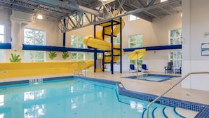 An indoor swimming pool with a yellow slide, blue steps, and a seating area with chairs.