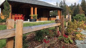 A rustic wooden building with a covered patio area, outdoor seating, and a garden with various plants and flowers.