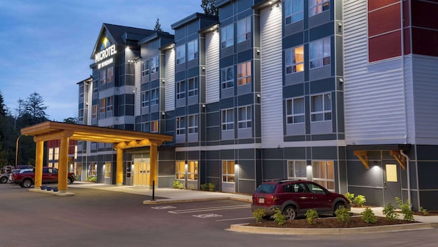 A multi-story hotel with a modern design, featuring a covered entrance and a parking area with a red car.
