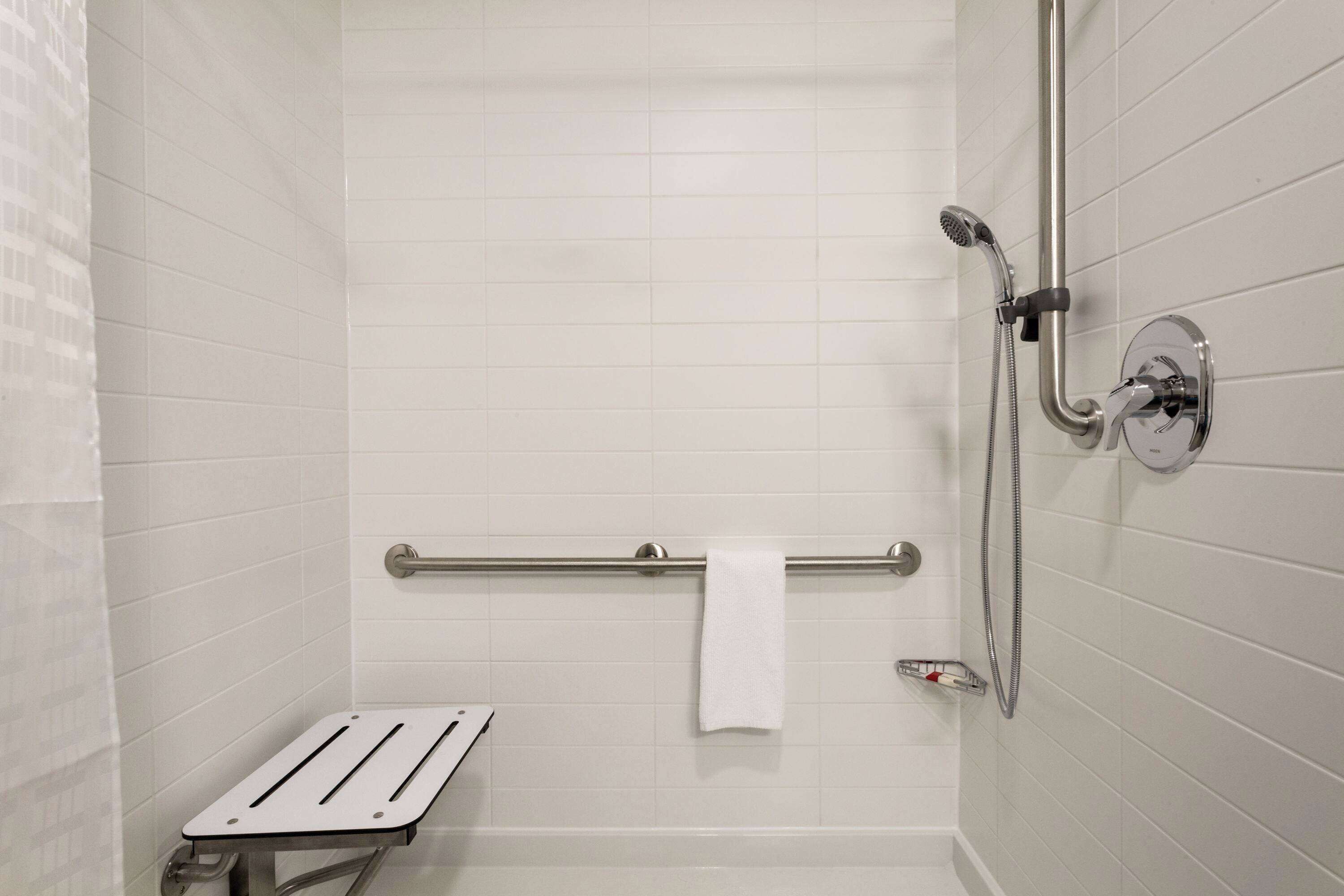 A bathroom with white tiled walls, a grab bar, a showerhead, and a towel rack.
