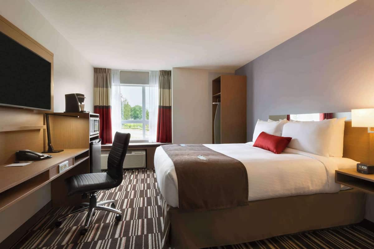 A hotel room with a bed, a desk with a chair, a TV, a wardrobe, and a window with curtains.