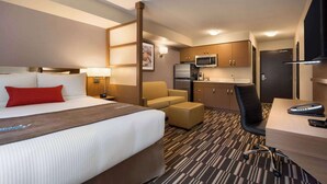A hotel room with a bed, a desk, a chair, a sofa, a microwave, a refrigerator, and a television.