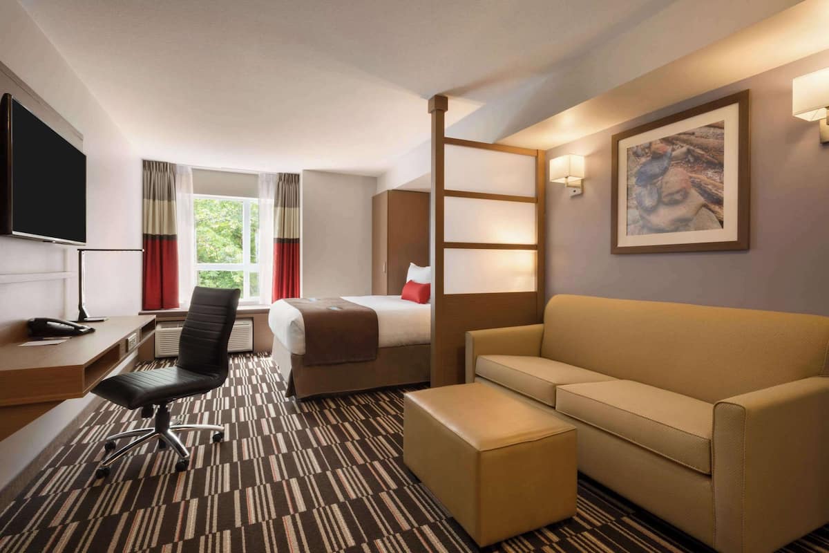 A hotel room with a bed, a sofa, a desk with a chair, a TV, and a window with curtains.