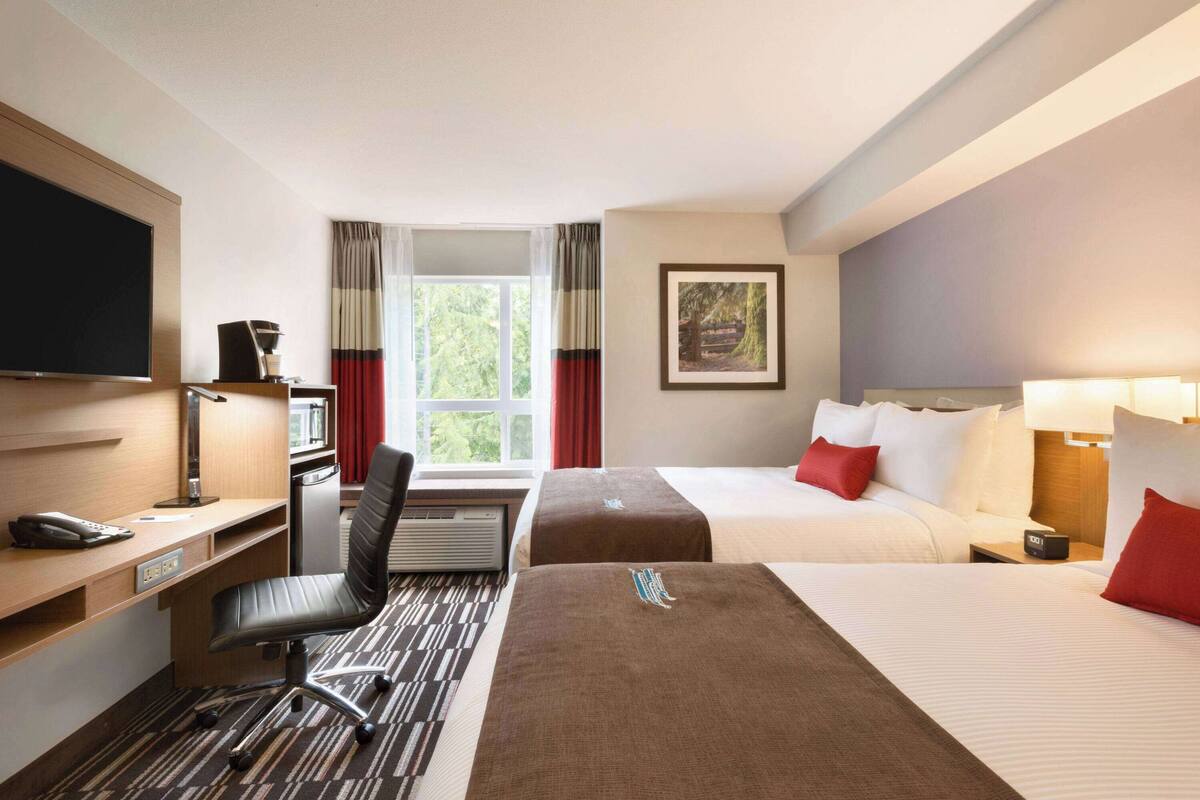A hotel room with a desk, two beds, a TV, and a window with curtains.