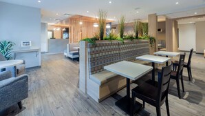 A modern restaurant with wooden flooring, a seating area with a bench and tables, and a counter with a menu display.