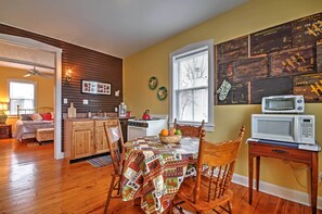 A cozy kitchen with wooden cabinets, a dining table with a quilt, and a microwave on a side table.