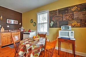 A kitchen with wooden cabinets, a dining table with a quilt, a microwave on a side table, and a window with blinds.
