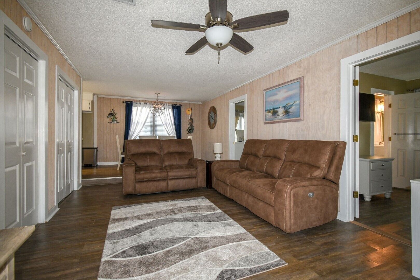 A spacious living room with a ceiling fan, a brown leather sofa, and a patterned rug.