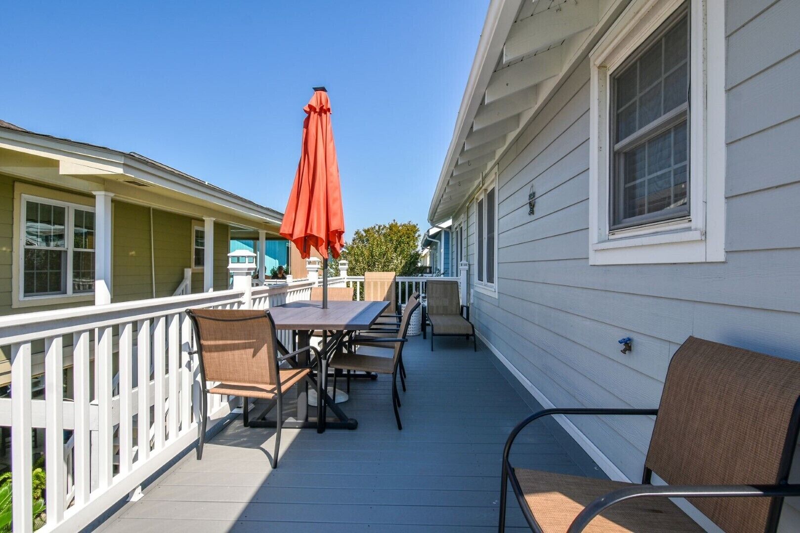 A covered outdoor patio with a table and chairs, a red umbrella, and a white railing.