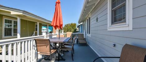 A covered outdoor patio with a table and chairs, a red umbrella, and a white railing.