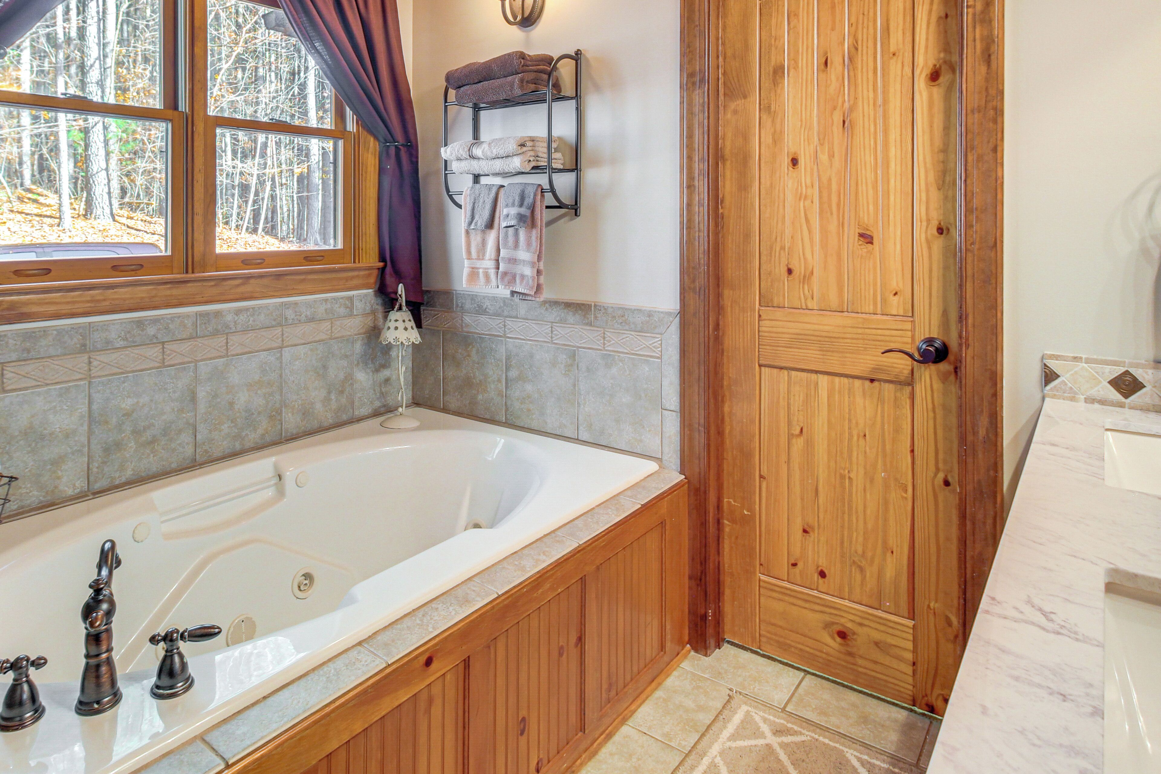 A bathroom with a wooden vanity, a large bathtub, and a window with curtains.