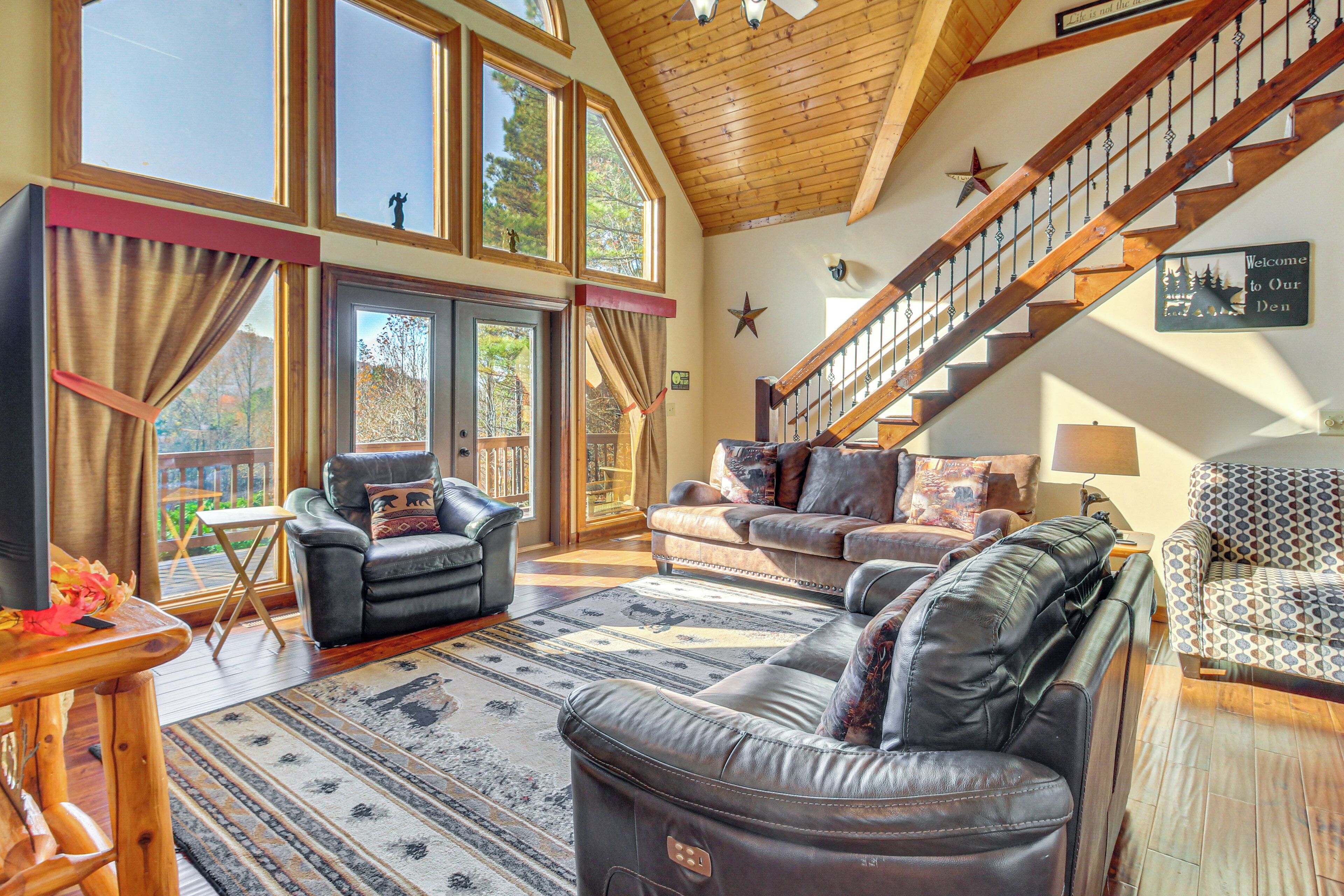 A spacious living room with leather sofas, a wooden staircase, and large windows.