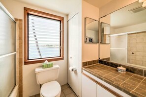 Une petite salle de bain comprenant des toilettes, une fenêtre avec stores, un miroir et un comptoir recouvert de carreaux.