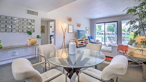 A modern living room with a glass table, four chairs, a sofa, a TV, and a large window with a view of the outdoors. - Rancho Mirage Condo on Fairway w/ Resort Amenities (Rancho Mirage)