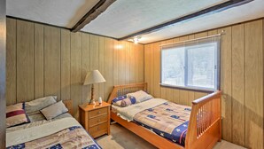 Une chambre avec deux lits simples, des têtes de lit en bois, une table de chevet avec une lampe et une fenêtre avec des stores.