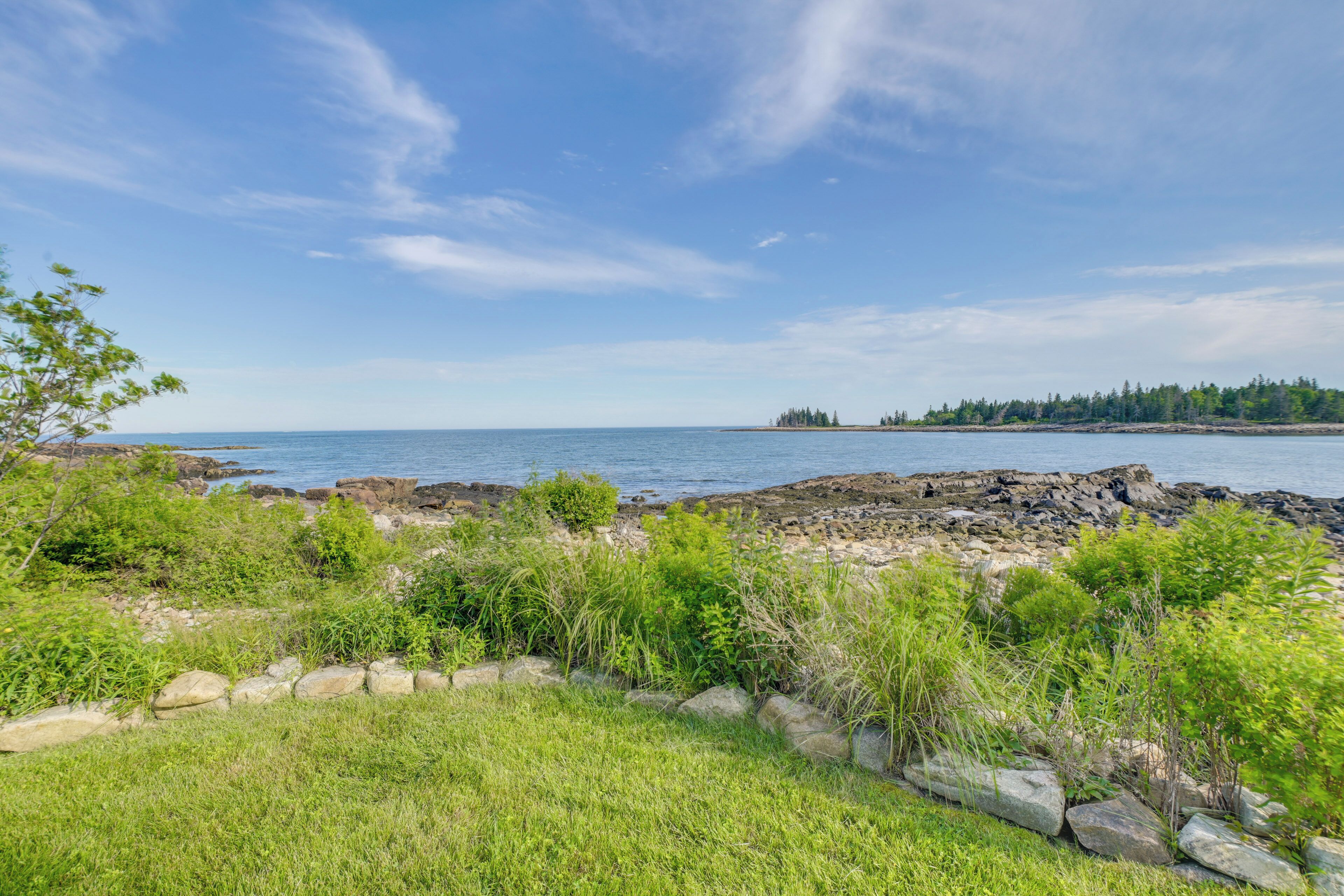 A coastal landscape with rocky terrain, greenery, and a clear sky.