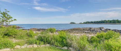 A coastal landscape with rocky terrain, greenery, and a clear sky.