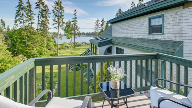 A deck with outdoor furniture, a potted plant, and a view of a lake and forest. - Waterfront Prospect Harbor Cottage: Yard, Fire Pit (Prospect Harbor)