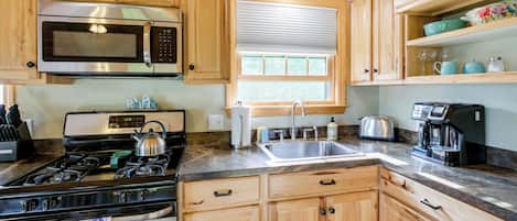 A kitchen with wooden cabinets, a stainless steel microwave, a gas stove, a sink, and a window with blinds.