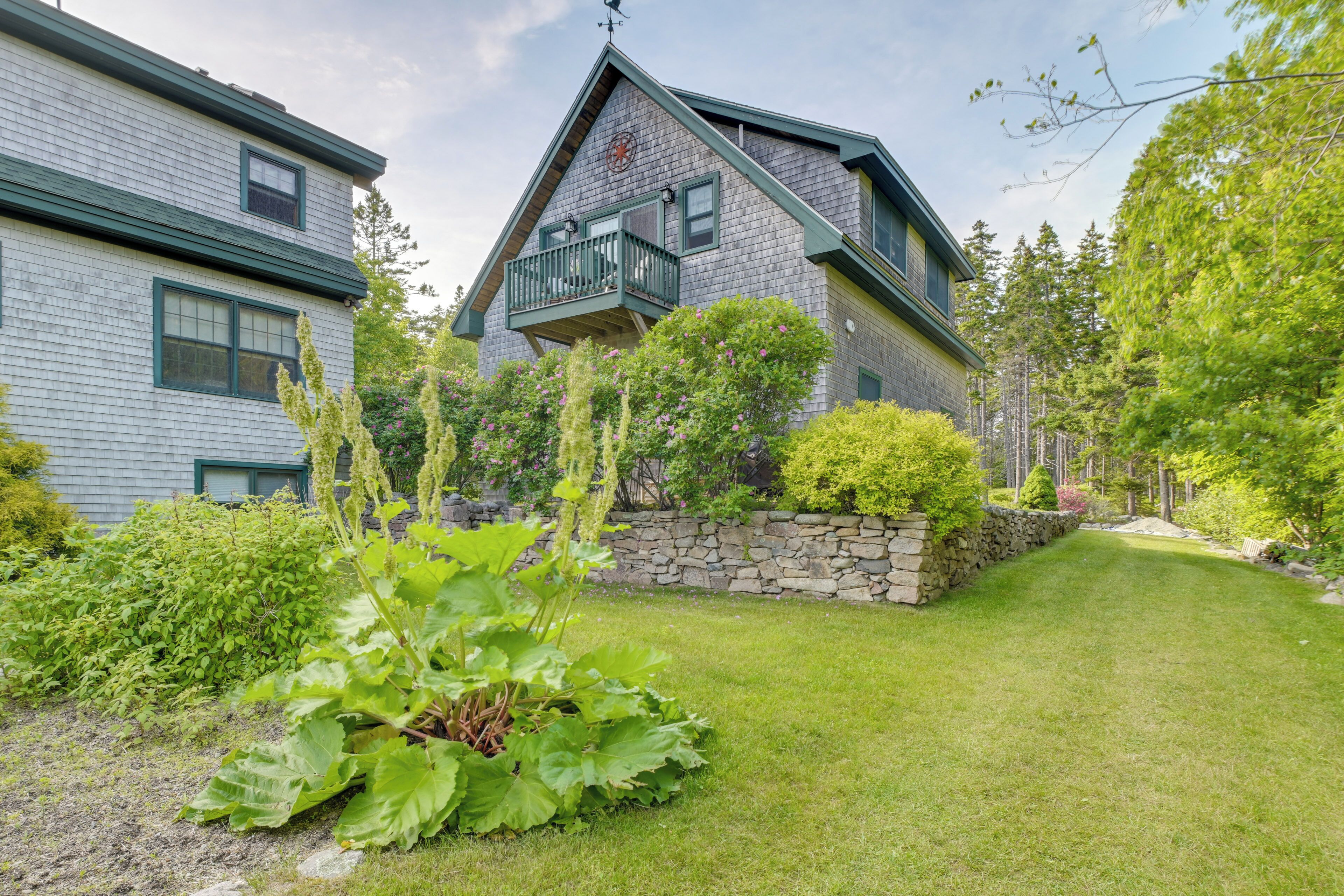 A two-story house with a stone wall, a balcony, and a well-maintained lawn.