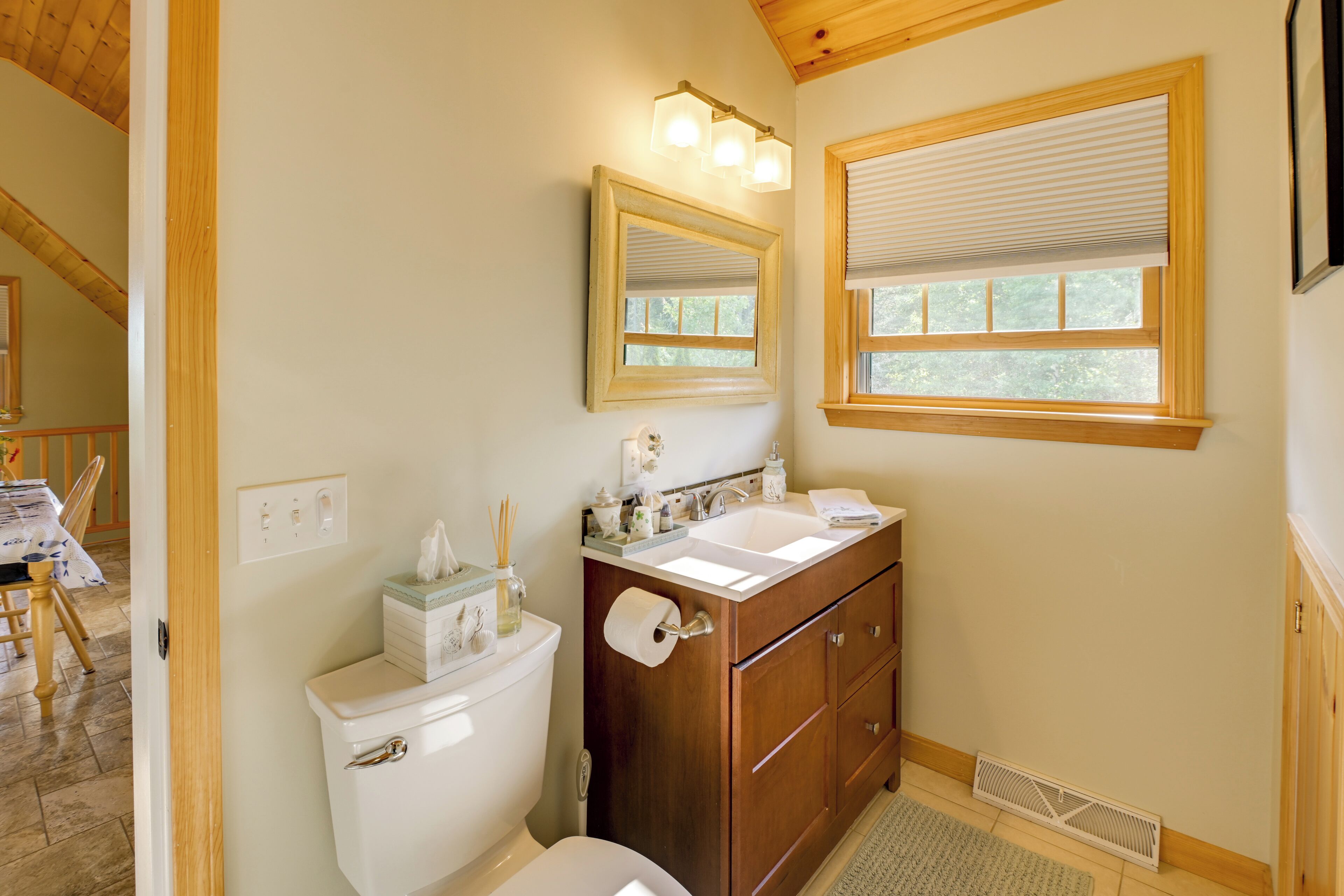 A bathroom with a toilet, sink, vanity, mirror, and window with blinds.