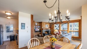 A cozy kitchen with wooden cabinets, a dining table with chairs, a chandelier, and a fireplace. - Nez Perce B1: Teton Village- Ground  Condo - Pool , Hot Tub Access (Teton Village)