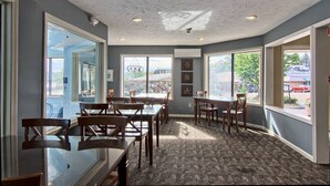 A restaurant interior with tables and chairs, large windows, and a ceiling with recessed lighting.