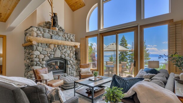 A cozy living room with a stone fireplace, comfortable seating, and large windows offering a view of the outdoors.