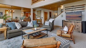 A spacious living area with a high ceiling, a dining area, and a kitchen. There is a staircase leading to an upper level.