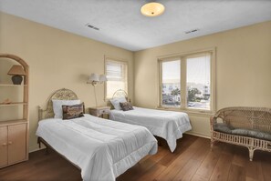 A bedroom with two beds, a wicker sofa, a nightstand, a lamp, and a view of the city.