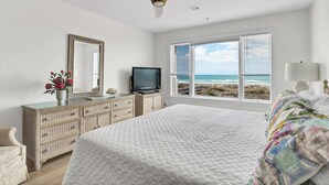 Un dormitorio con una cama grande, un aparador, un televisor y una ventana con vistas a la playa.
