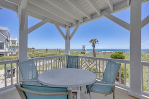 A covered outdoor area with a table and chairs, overlooking a beach and ocean.